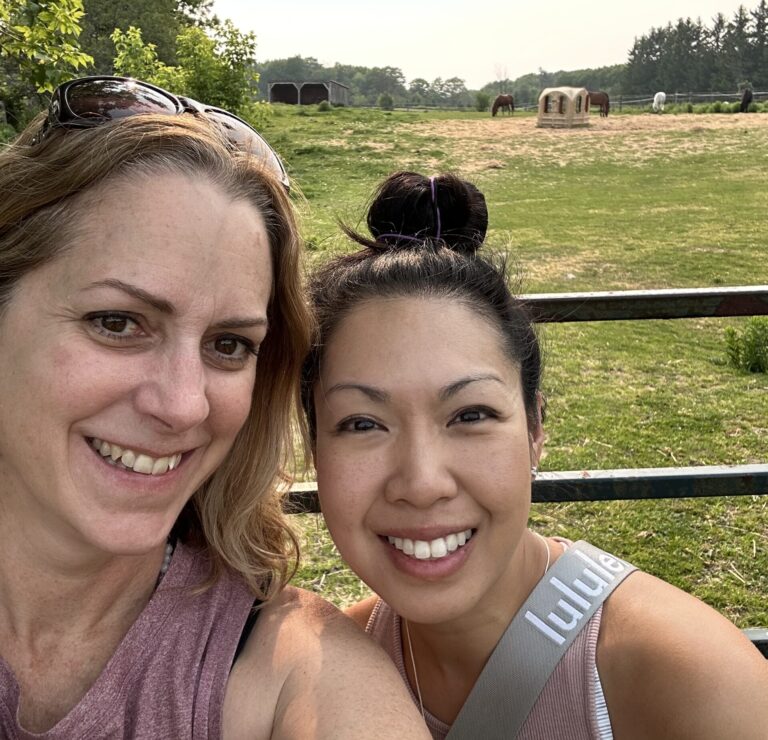Dr. Jessica and Catherine smiling at the camera with horses in the background.