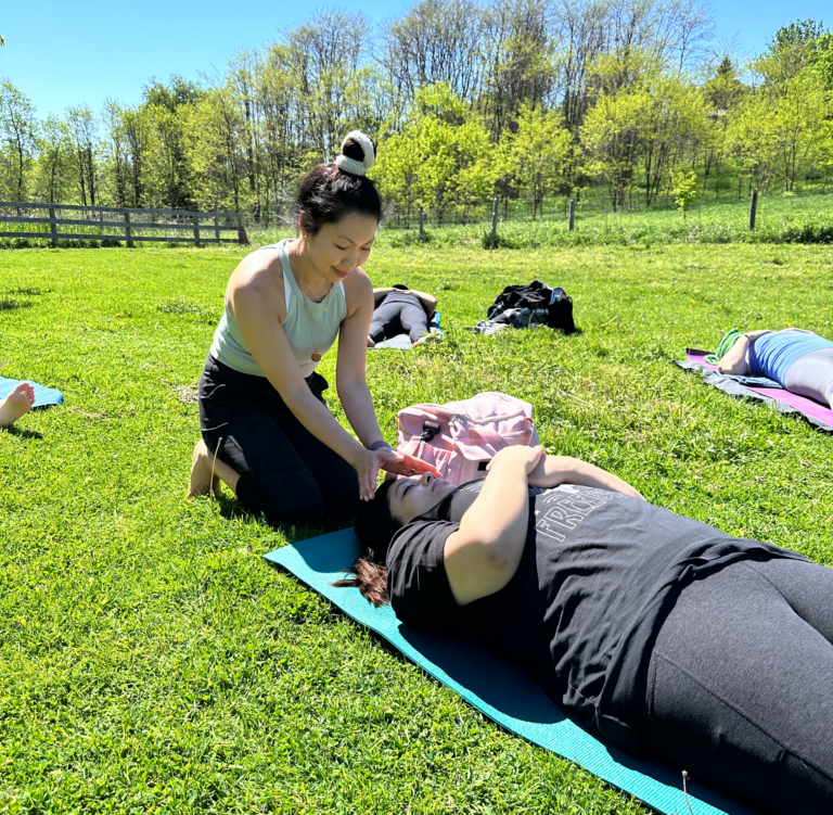 Dr. Jessica doing reiki on woman laying on the grass in a field.