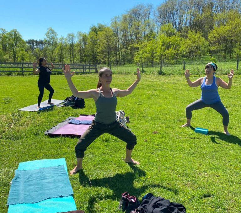 Women doing yoga in a field in Goddess Pose.